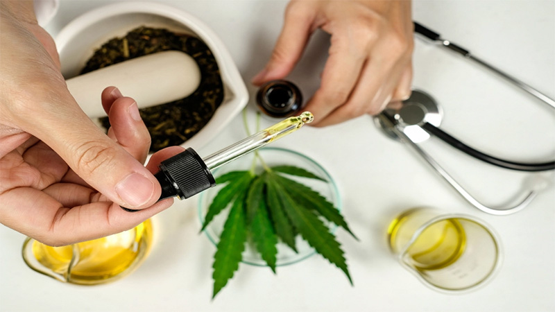 Image of hand getting CBD oil from the bottle with hemp leaves and stethoscope on the background