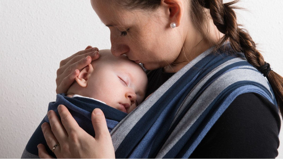 A Mother Kissing Her Baby's Head While Carrying Through Babywearing