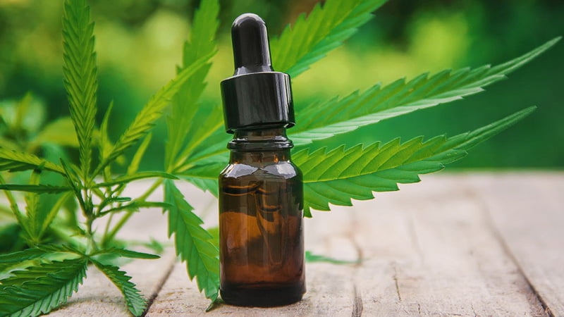 CBD Oil Standing on a Wooden Surface with Hemp Leaves