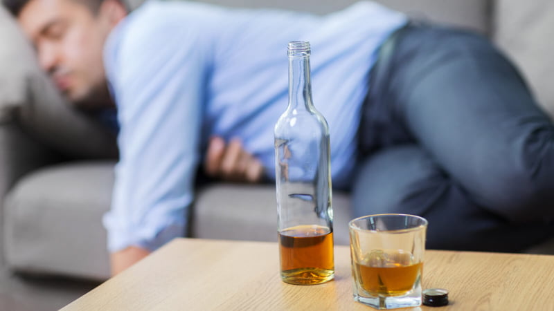 Man on the Couch with Hangover while a Bottle and Glass of Whisky in the Table
