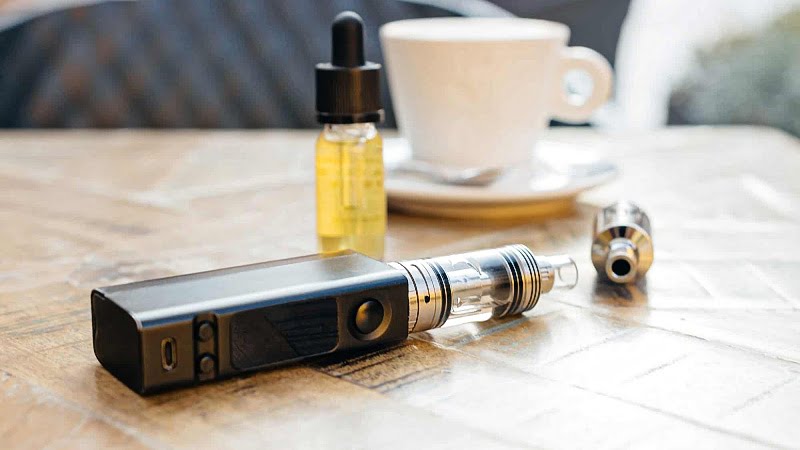 CBD vape oil, e-cigarette and a cup placed on the table