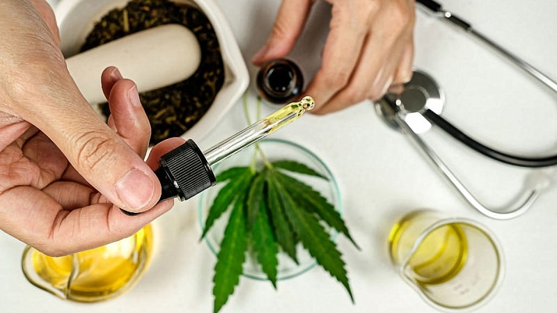 a doctor taking CBD oil dropper with CBD oil extract, stethoscope, hemp leaves and seeds