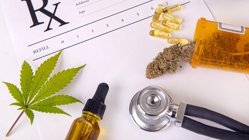 Cannabis leaf, a bottle of CBD oil, stethoscope, capsules and a container of hemb buds placed at the top of a medical prescription paper