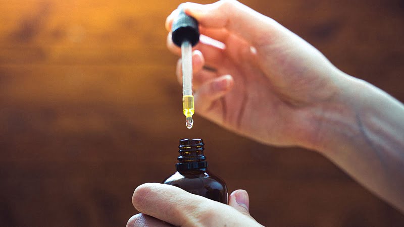 a hand taking CBD oil extract using a dropper