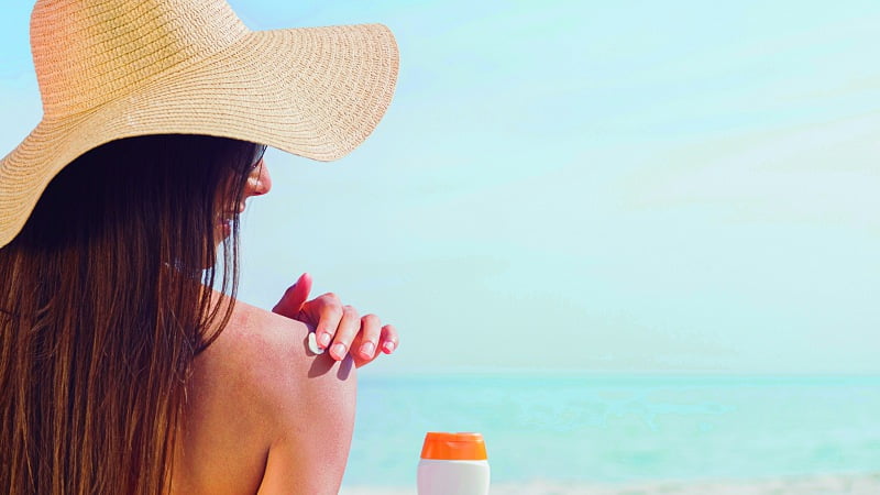 a woman at the beach applying CBD sunscreen onto her own shoulder