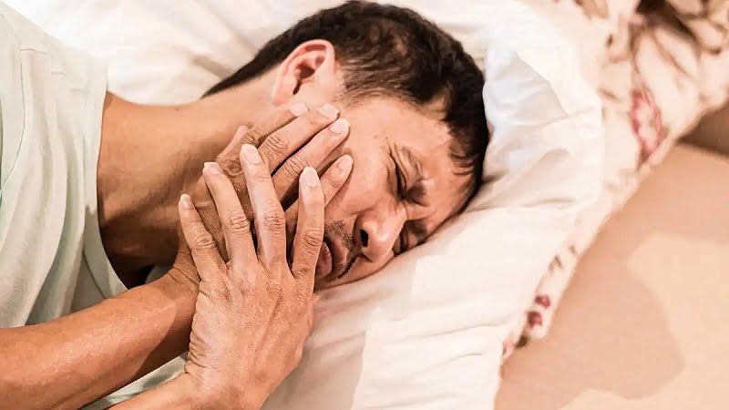 a man suffering from TMJ disorder while lying in bed