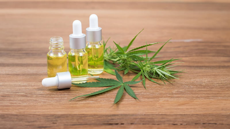Three CBD Oil Bottles with Hemp Leaves on a Wooden Surface