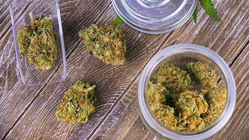 top view image of hemp buds on a container and other pieces scattered on the wooden table