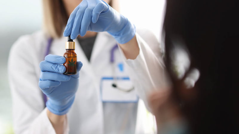 Doctor Wearing Blue Gloves Holding CBD Oil In-front of a Patient