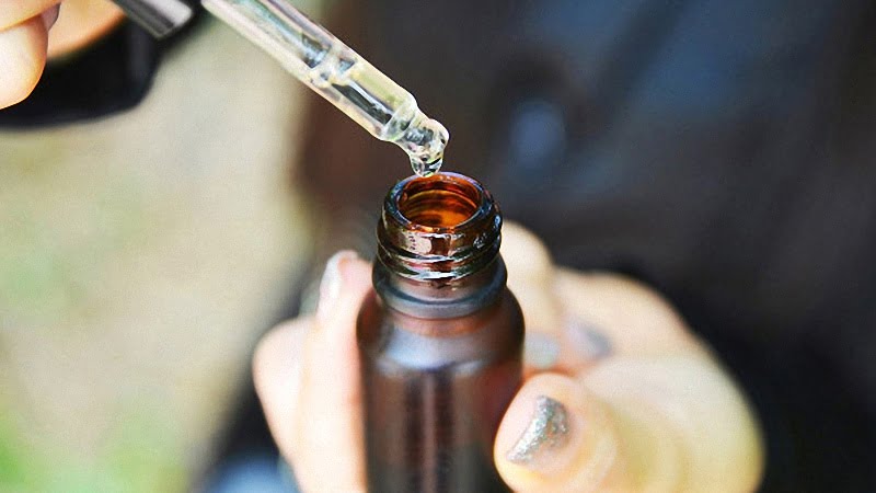 Hand Holding CBD Oil Dropper and Bottle