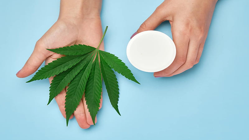 hand holding hemp leaf and cbd cream for feet