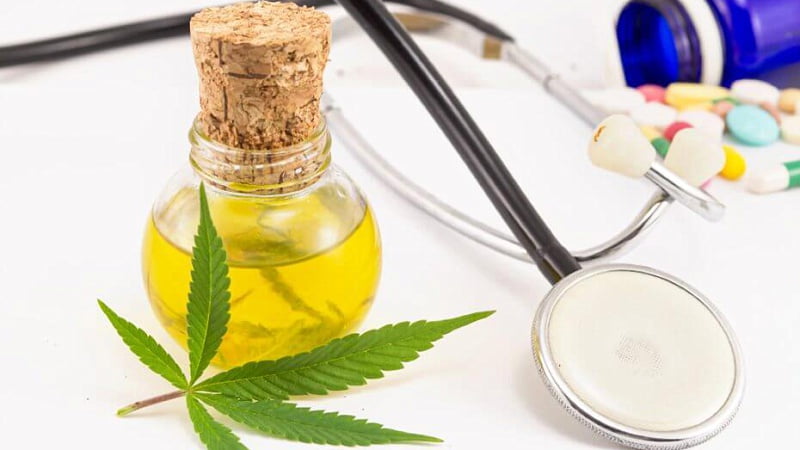 a bottle of CBD oil with a hemp leaf leaning on it, a stethoscope, and some medicines