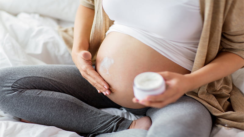 Pregnant Woman Applying CBD Cream to Stomach while Holding It