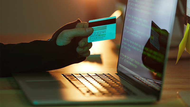 Image of a guy holding a credit card in front of laptop