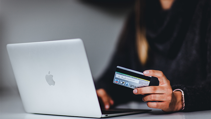 Image of a Person holding a Card and using the Laptop