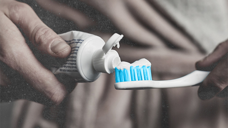 Una persona poniendo pasta de dientes en el cepillo de dientes.