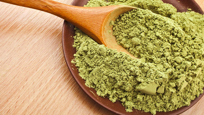Green Borneo Kratom powder on a plate with a wooden spoon