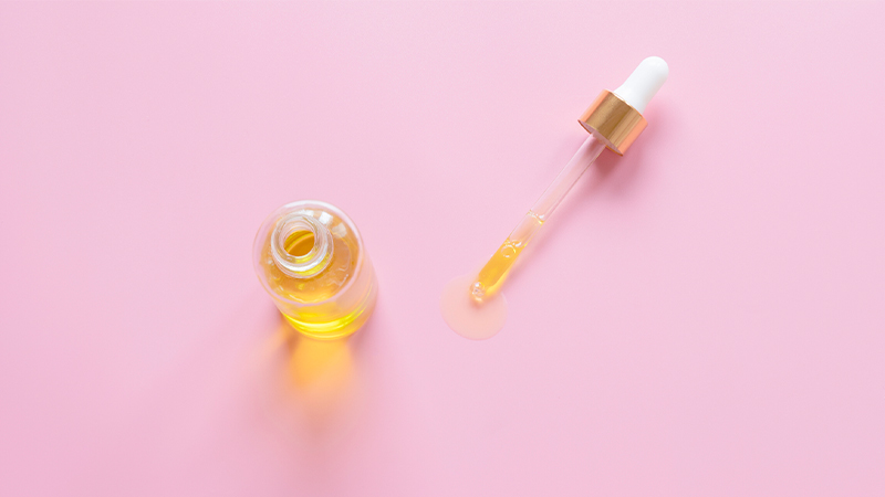 CBD oil in a bottle with a dropper on the side in pink background