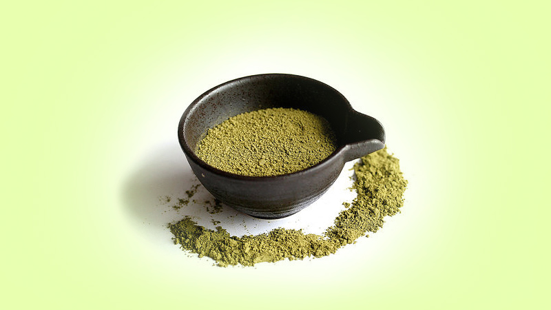 Kratom powder in container in light green background