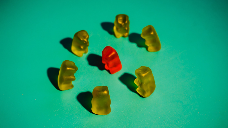 Six green gummies looking at a red gummy