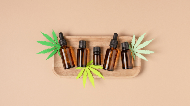 Top view of various bottles of CBD oil with hemp leaves in light brown background